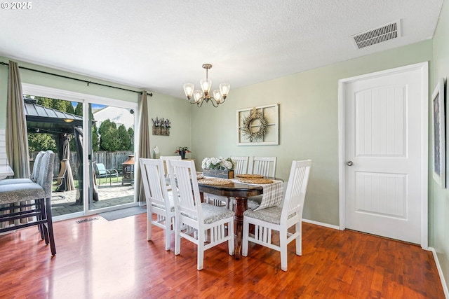 dining space featuring an inviting chandelier, a textured ceiling, visible vents, and wood finished floors