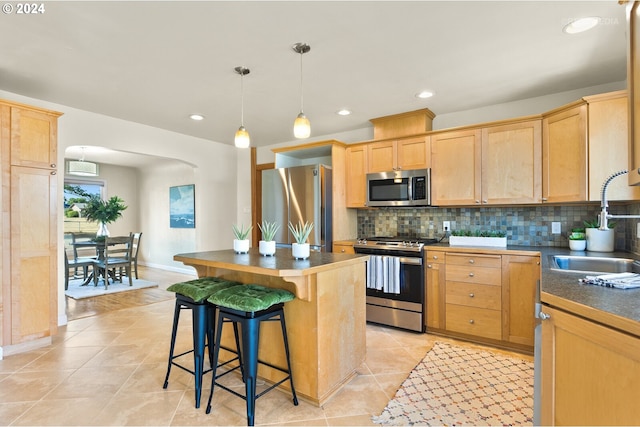 kitchen featuring light brown cabinets, hanging light fixtures, sink, appliances with stainless steel finishes, and a kitchen island