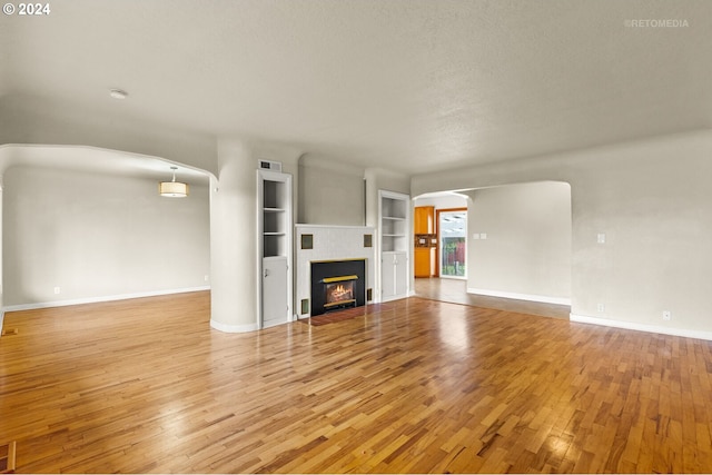 unfurnished living room featuring built in shelves, wood-type flooring, and a textured ceiling