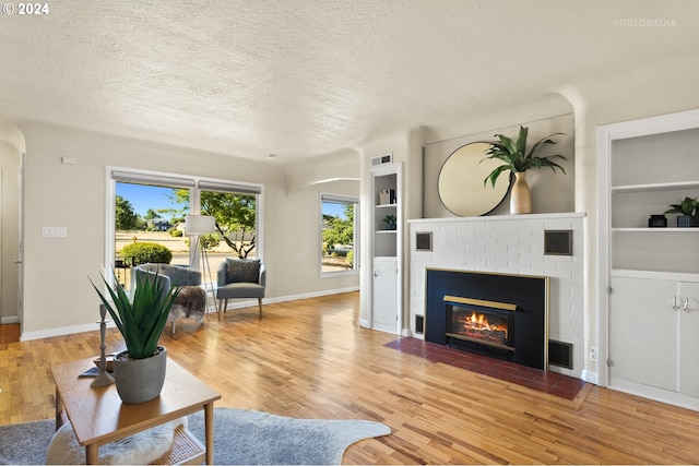 living room featuring hardwood / wood-style flooring, built in features, a textured ceiling, and a brick fireplace