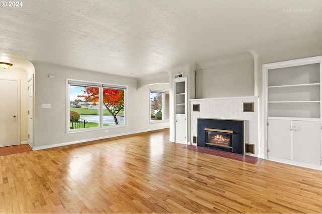 unfurnished living room featuring built in features, a textured ceiling, light hardwood / wood-style floors, and a brick fireplace