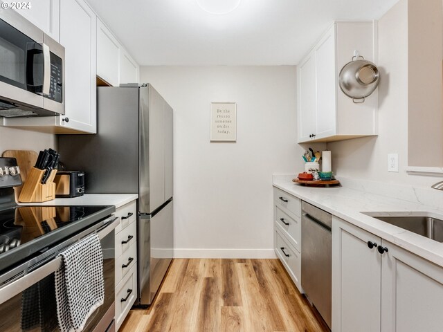 kitchen with light hardwood / wood-style floors, stainless steel appliances, sink, light stone counters, and white cabinets