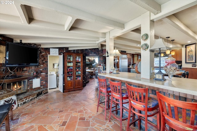 kitchen featuring a brick fireplace, a textured ceiling, beamed ceiling, washer / clothes dryer, and hanging light fixtures