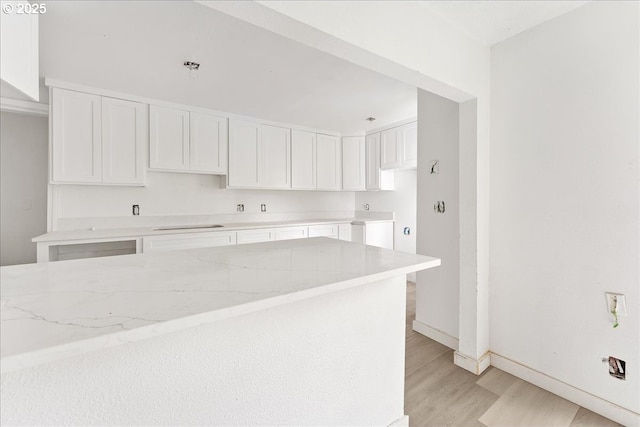 kitchen featuring light stone countertops, light hardwood / wood-style floors, and white cabinets