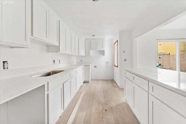 kitchen featuring white cabinetry, light stone countertops, sink, and light hardwood / wood-style floors