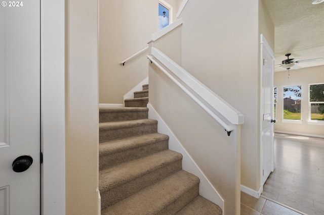 staircase with ceiling fan, a textured ceiling, and light hardwood / wood-style floors