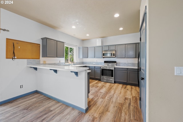 kitchen featuring appliances with stainless steel finishes, kitchen peninsula, gray cabinets, light wood-type flooring, and a breakfast bar