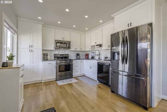 kitchen with white cabinetry, sink, light hardwood / wood-style flooring, backsplash, and appliances with stainless steel finishes