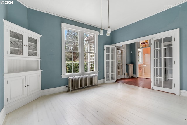 empty room featuring radiator heating unit, ornamental molding, light wood-type flooring, and french doors