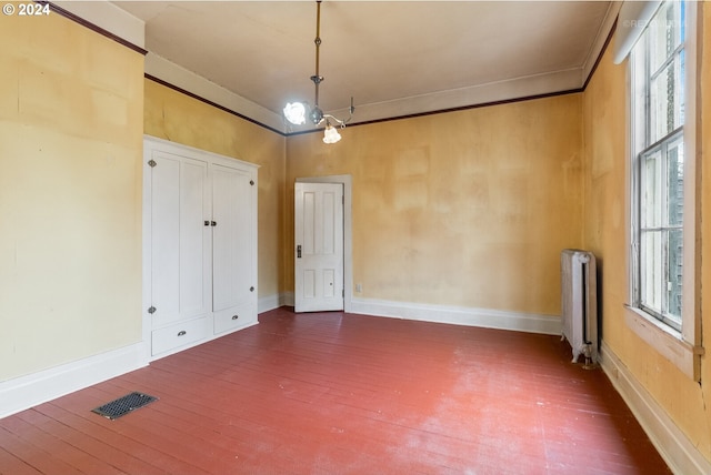 empty room featuring radiator heating unit, crown molding, dark hardwood / wood-style floors, and an inviting chandelier