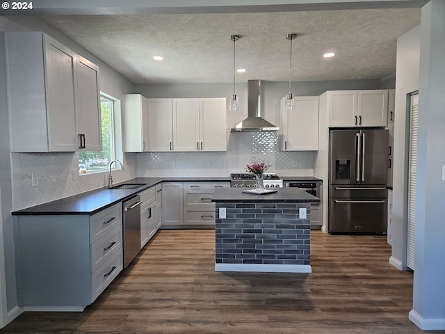 kitchen with appliances with stainless steel finishes, white cabinetry, decorative light fixtures, and wall chimney exhaust hood