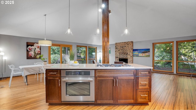 kitchen featuring pendant lighting, lofted ceiling, light hardwood / wood-style flooring, stainless steel appliances, and a center island with sink