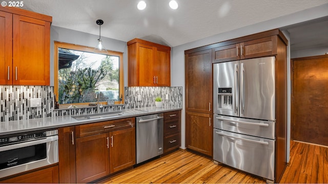 kitchen featuring pendant lighting, stainless steel appliances, tasteful backsplash, sink, and light hardwood / wood-style flooring