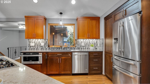 kitchen featuring light stone countertops, tasteful backsplash, sink, pendant lighting, and stainless steel appliances