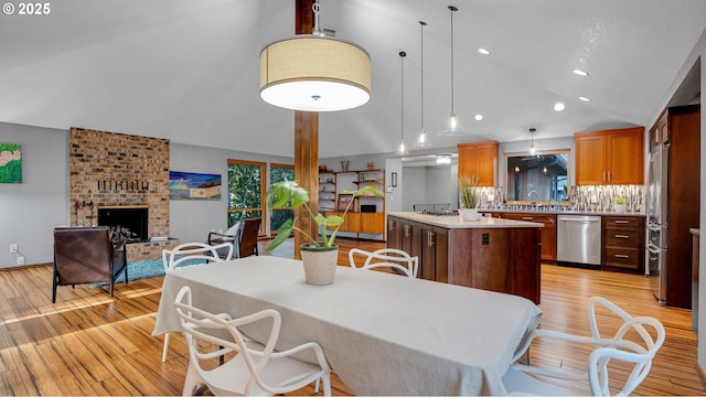 kitchen featuring a brick fireplace, stainless steel appliances, decorative backsplash, hanging light fixtures, and a center island