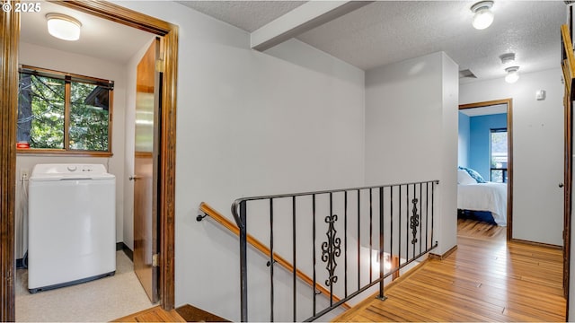 corridor with plenty of natural light, a textured ceiling, light wood-type flooring, and washer / clothes dryer