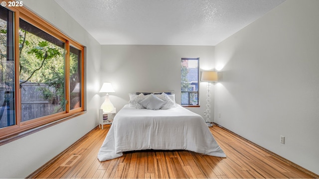 bedroom with a textured ceiling, hardwood / wood-style flooring, and multiple windows