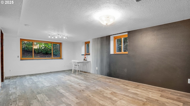 spare room featuring track lighting, light hardwood / wood-style flooring, and a textured ceiling