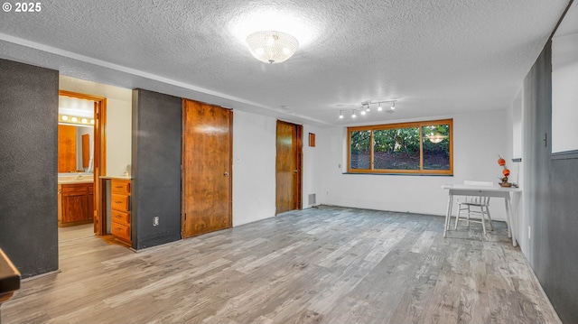 unfurnished living room with light wood-type flooring, track lighting, and a textured ceiling