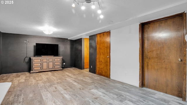 unfurnished living room with light wood-type flooring, track lighting, and a textured ceiling