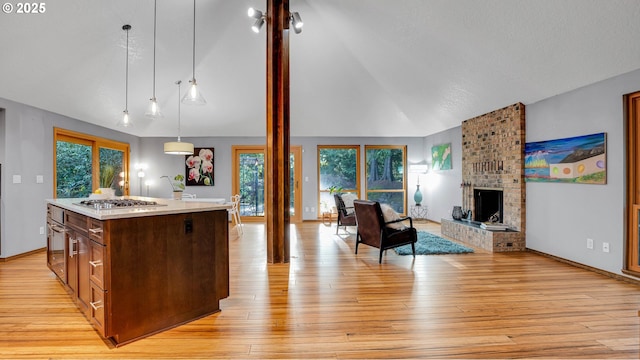 kitchen with lofted ceiling, an island with sink, hanging light fixtures, stainless steel gas cooktop, and a brick fireplace