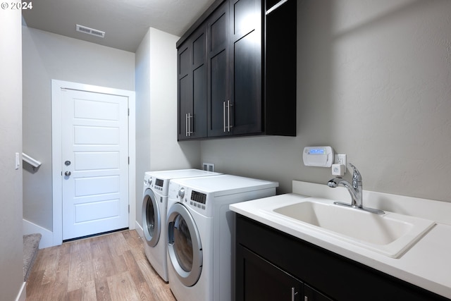 laundry area with light hardwood / wood-style floors, cabinets, sink, and washing machine and dryer