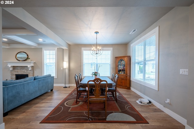 dining room with hardwood / wood-style floors, a notable chandelier, beam ceiling, and a fireplace