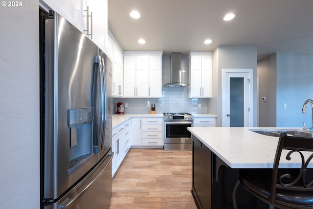 kitchen featuring a kitchen breakfast bar, white cabinetry, wall chimney range hood, and stainless steel appliances