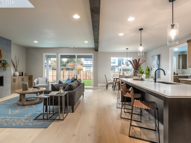 living room featuring beam ceiling, light wood-type flooring, a tiled fireplace, and sink