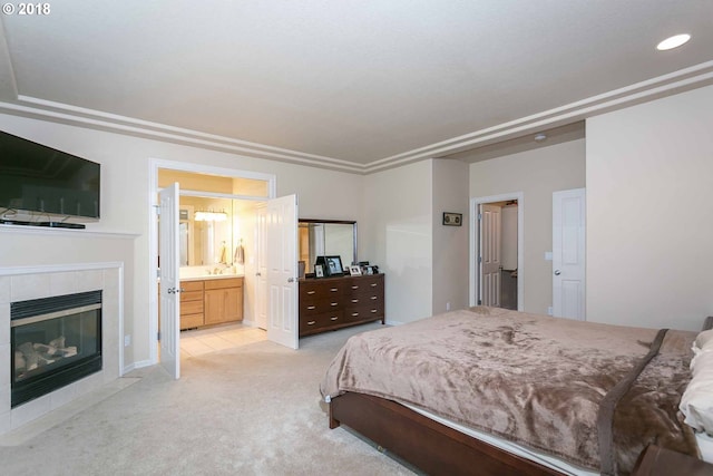 bedroom featuring light carpet, a tiled fireplace, ensuite bath, and recessed lighting