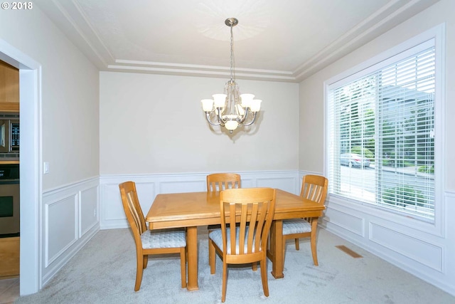dining room with a chandelier, light carpet, wainscoting, and a decorative wall