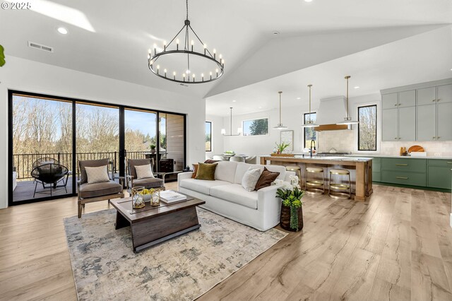 living room with high vaulted ceiling, a notable chandelier, a fireplace, and light hardwood / wood-style flooring