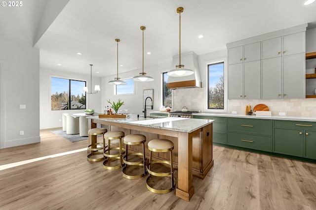 kitchen featuring light wood finished floors, backsplash, stove, a kitchen island with sink, and a kitchen breakfast bar