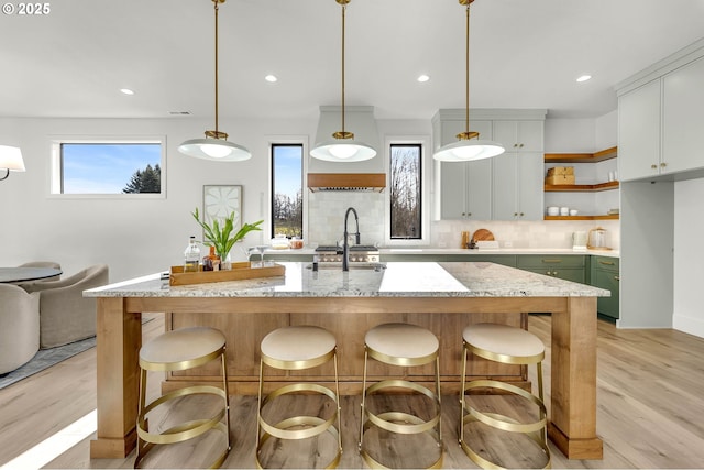 kitchen with a breakfast bar area, backsplash, open shelves, an island with sink, and decorative light fixtures