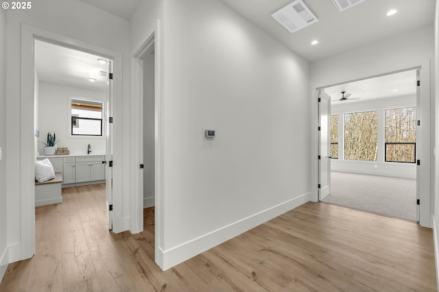 hallway with light wood-style floors, baseboards, a sink, and recessed lighting