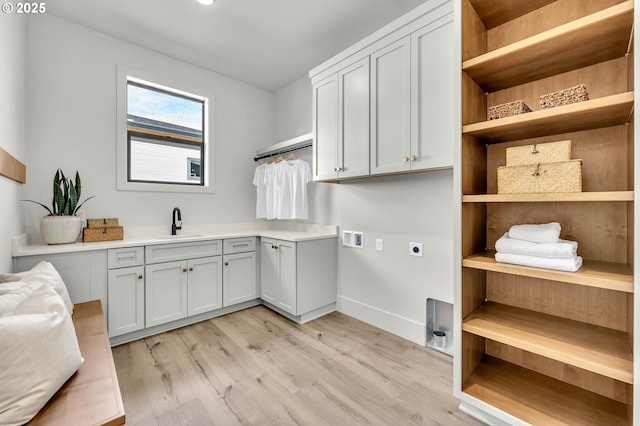 washroom with hookup for an electric dryer, washer hookup, a sink, cabinet space, and light wood finished floors