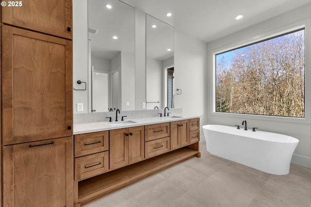 full bath featuring recessed lighting, a freestanding tub, a sink, and double vanity