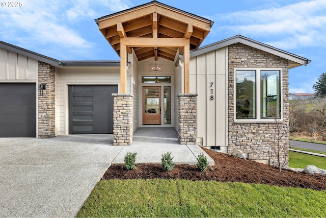 property entrance with board and batten siding, stone siding, driveway, and an attached garage