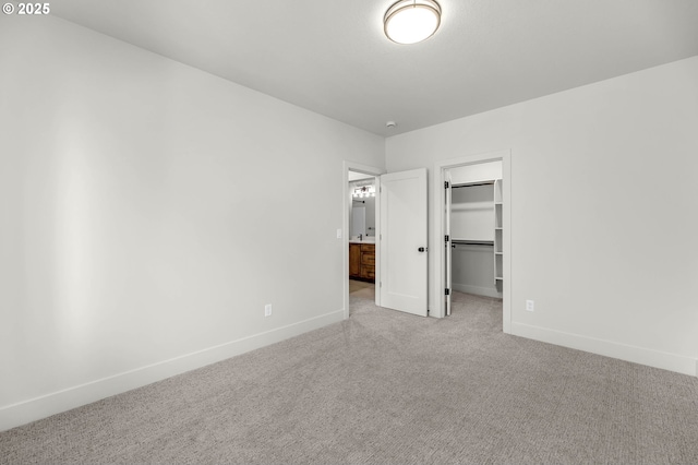 unfurnished bedroom featuring a spacious closet, baseboards, a closet, and light colored carpet