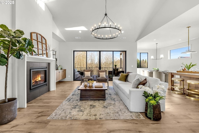 living area featuring a chandelier, light wood-type flooring, high vaulted ceiling, and a tiled fireplace