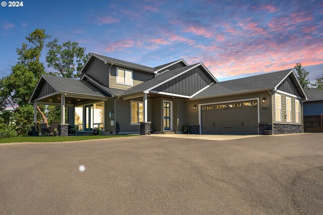 craftsman inspired home with board and batten siding, a garage, a shingled roof, driveway, and stone siding