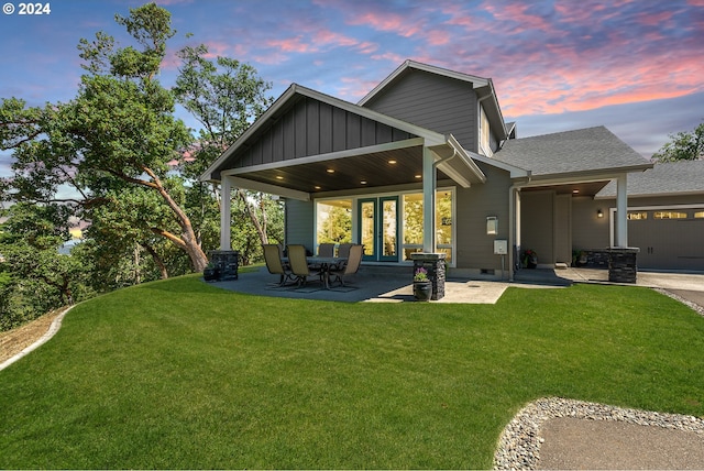 rear view of property featuring a lawn, an attached garage, french doors, and board and batten siding