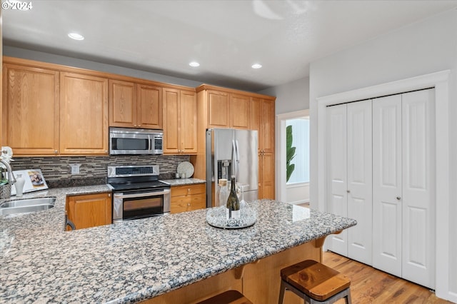 kitchen featuring a breakfast bar, sink, decorative backsplash, stainless steel appliances, and light stone countertops