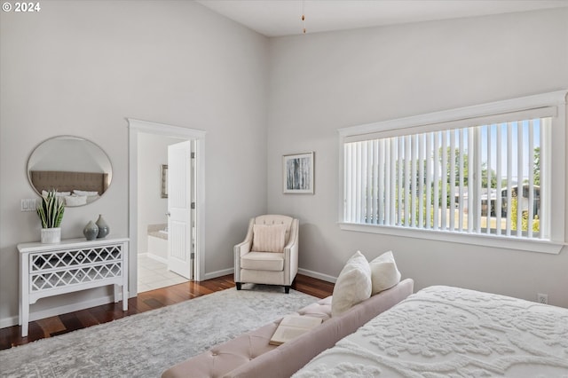 bedroom with a towering ceiling, wood-type flooring, and connected bathroom