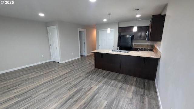 kitchen with sink, hanging light fixtures, dark wood-type flooring, black fridge, and kitchen peninsula