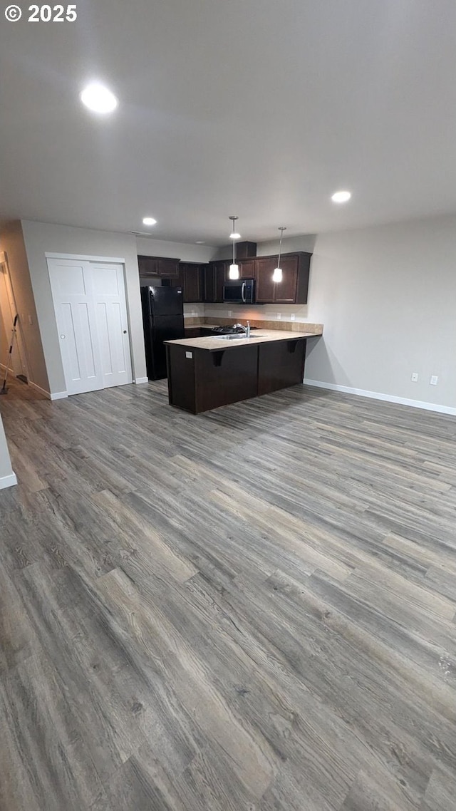 kitchen featuring black refrigerator, kitchen peninsula, a breakfast bar, wood-type flooring, and hanging light fixtures