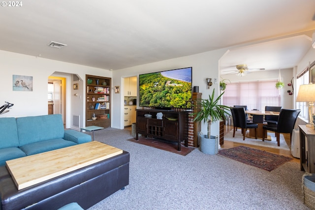 carpeted living room featuring built in shelves and ceiling fan