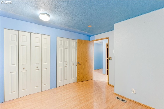 unfurnished bedroom with light hardwood / wood-style flooring, a textured ceiling, and two closets