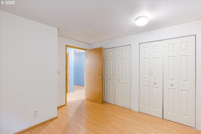 unfurnished bedroom featuring light wood-type flooring, a textured ceiling, and two closets