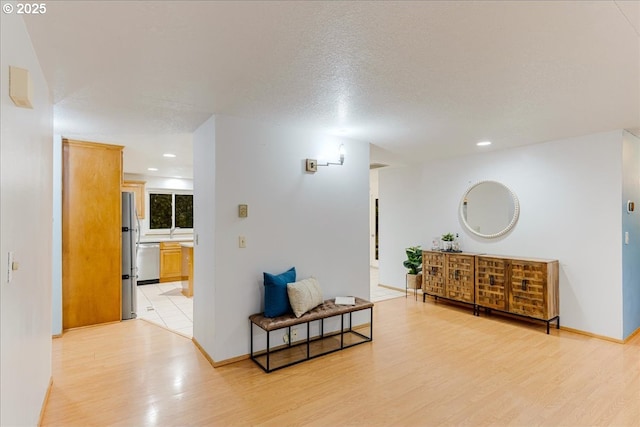 hall with sink, light wood-type flooring, and a textured ceiling